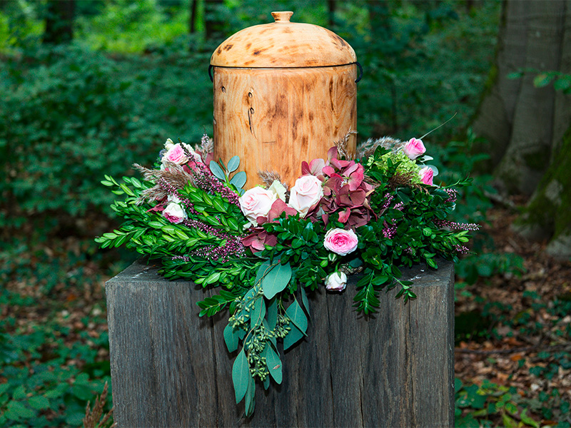 Waldbestattung mit Holzurne und Blumenschmuck als natürliche Form des Abschieds von einem geliebten Menschen in ruhiger Waldumgebung.