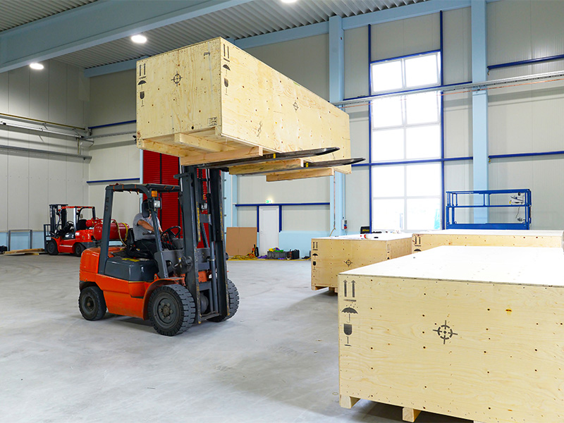 Gabelstapler transportiert schweren Verschlag aus Holz mit Maschinenbauteilen in einer Industriehalle f&uuml;r den sicheren Versand.