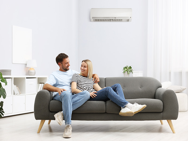 Paar sitzt gemeinsam auf Sofa in Wohnraum mit eingeschalteter Klimaanlage und verbringt entspannt Zeit im Wohnzimmer.